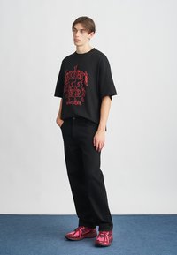 T-shirt oversized preta com impressão gráfica vermelha, combinada com jeans pretos e sapatilhas de corrida rosas com detalhes pretos e tecido texturizado.