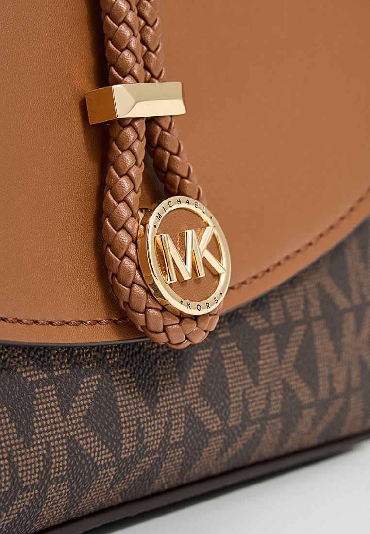 Braune Lederhandtasche mit geflochtenem Griff, goldenen Akzentbeschlägen und einem strukturierten MK-Logo auf einem dunkleren gemusterten Hintergrund.