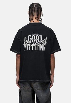 Black oversized t-shirt featuring a large white graphic with text and butterfly motifs on the back. Visible contrasting stitching details.