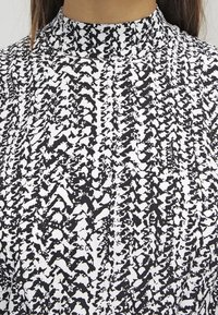 Black and white patterned fabric with a high neck design, featuring an abstract texture and a blend of shapes across the surface.