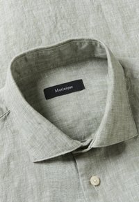 Chemise en lin vert clair avec un col à pointes écartées et un bouton visible, arborant une étiquette de marque Matinique noire à l'intérieur du col.