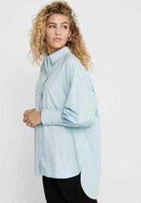 Camicia azzurra oversize con bottoni, colletto a punta, maniche arricciate e orlo curvo. Tessuto in cotone con una texture liscia.
