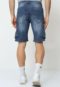 Shorts cargo en denim, bleu avec une finition délavée. Comprend des poches cargo latérales et des poches arrière traditionnelles. Coupés juste au-dessus du genou.