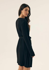 Czarna sukienka z długimi rękawami i paskiem w talii, wykonana z miękkiego, gładkiego materiału. Posiada luźny krój i zwiewny dół.