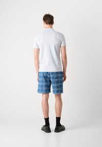 Λευκό κοντομάνικο πόλο πουκάμισο, τζιν σορτς με μπλε καρό σχέδιο, μαύρες κάλτσες και μαύρα παπούτσια, φαίνεται από πίσω.