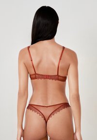 Set di lingerie in pizzo rosso con spalline regolabili, intricate fantasie floreali e pannelli trasparenti. La parte posteriore presenta un delicato bordo a scallop.