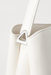 White leather handbag featuring a triangular silver hardware accent where the strap attaches, showcasing a smooth texture.