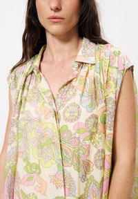 Bluse mit Blumenmuster in Pastellfarben, aus weichem Stoff, mit spitzem Kragen und kurzen Ärmeln. Knöpfe am Hals fügen Details hinzu.