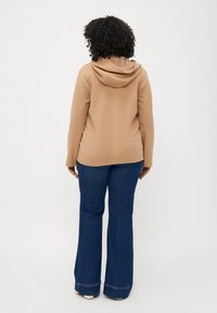 Καστανή κουκούλα με χαλαρή εφαρμογή, συνδυασμένη με καμπάνα τζιν μπλε, που διαθέτει κλασικό σχέδιο πέντε τσέπες και φθαρμένο στρίφωμα.