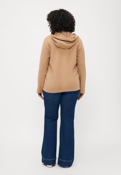 Sweatshirt à capuche beige avec une coupe décontractée, associé à un jean en denim bleu évasé, présentant un design classique à cinq poches et un ourlet effiloché.
