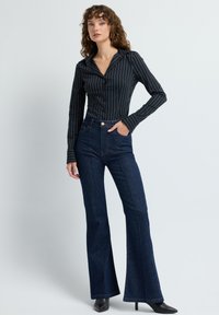 Černobílá pruhovaná košile na knoflíky s přiléhavým střihem a dlouhými rukávy, doplněná tmavě modrými rozšířenými džínami a černými lodičkami na jehlovém podpatku.