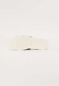 Svart sandal såle med en teksturert hvit gummibase. Har vekslende glatte og ribbede mønstre for godt grep. Minimalistisk design.