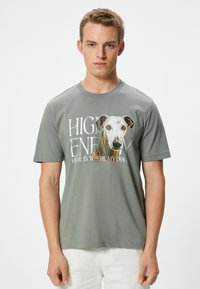 Camiseta gris de manga corta con un gran gr�áfico de perro y el texto "EN CASA CON ALTA ENERGÍA ES DONDE ESTÁ MI PERRO". Material de algodón suave, ajuste relajado.