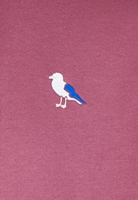 Maroon fabric with a textured finish featuring an embroidered bird design in white and blue, positioned on the lower left.