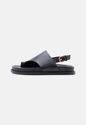 Sort læder sandal med åben tå, bred rem, slingback-ankelrem med guldlås og flad sål på en ensfarvet lys baggrund.