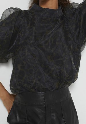 Czarna przezroczysta bluzka z bufkami i subtelnym wzorem w panterkę, zestawiona z czarnymi, wysokim stanem, skórzanymi spodniami na osobie.