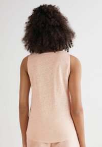 Ljusrosa ärmlös topp med rundad halsringning, tillverkad av mjukt tyg. Designen har en subtil textur och en avslappnad passform.