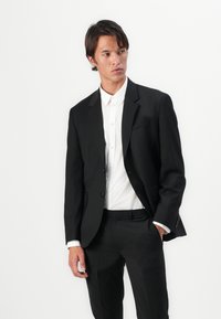 Black tailored suit jacket with notch lapels, single-button closure, and two pockets, paired with a white button-up shirt.