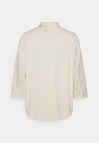 Beiges Baumwollhemd mit Kragen, langen Ärmeln und Knopfdetails. Die Rückseite hat einen abgerundeten Saum und eine lockere Passform.