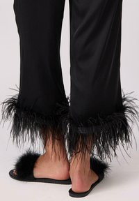 Czarne satynowe spodnie z piórkowymi akcentami na końcach, w połączeniu z czarnymi klapkami z futrzanymi detalami na wierzchu.
