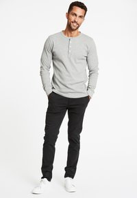 Graues Langarm-Henley-Shirt mit Rundhalsausschnitt und drei Knöpfen, kombiniert mit schwarzen Hosen und weißen Turnschuhen. Schlichte Textur.
