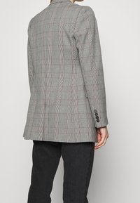 Blazer de cuadros gris con ajuste entallado, solapas con muescas, puños de tres botones y una abertura en la espalda para mayor estilo.