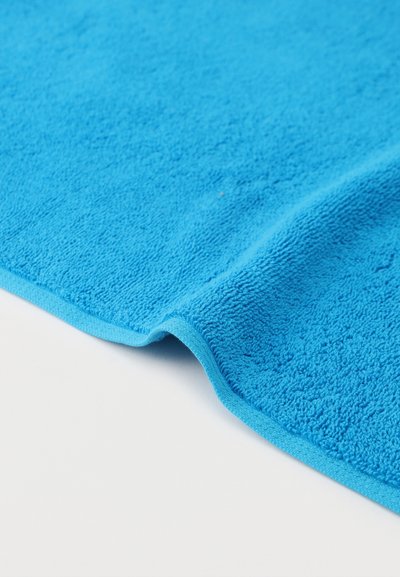 Φωτεινή μπλε πετσέτα από περκάλι με λεπτομέρειες υφής, διπλωμένη ελαφρώς πάνω σε λευκή επιφάνεια.