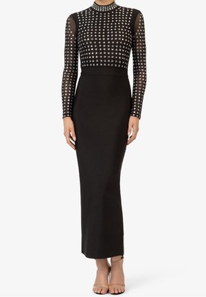 Vestido largo negro de manga larga con adornos cuadrados plateados en el corpiño y las mangas, cintura ajustada y falda hasta el tobillo, combinado con tacones nude.