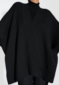 Zwarte gebreide poncho met een gestructureerd patroon, oversized ontwerp en open voorkant. Voorzien van een geribde halslijn en subtiele glans.