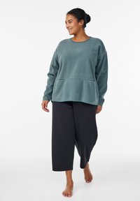 Zelenomodrý flísový sveter s zaobleným výstrihom a našnurovaným pásom, v kombinácii s voľnými čiernymi nohavicami, oba majú mäkké textúry.