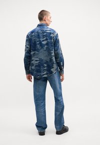 Jeanshemd in verschillende blauwtinten met een gestructureerde afwerking, voorzien van een relaxte pasvorm, lange mouwen en logoaccenten. Gecombineerd met lichtblauwe jeans.