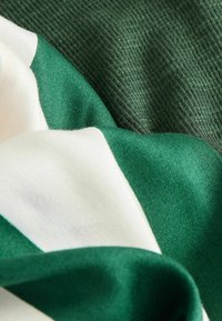 Silk fabric in deep green and cream, featuring smooth and textured sections, with a wavy layout highlighting color contrasts.