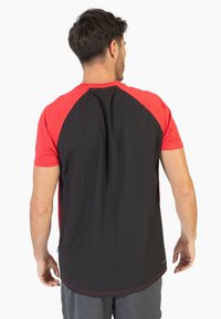 Camiseta atlética de manga corta con la parte superior roja y la parte inferior negra. Presenta un patrón en la tela y una espalda ventilada para mayor transpirabilidad.