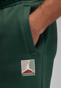 Grüne Jogginghose aus weichem Stoff mit seitlichen Taschen und elastischem Bund. Mit einem Jordan-Logo in Weiß sowie rosa und grünen Akzenten.