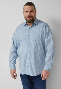 Lichtblauw overhemd met kleine bloemenprint, lange mouwen en een klassieke kraag. Gecombineerd met donkerblauwe spijkerbroek.