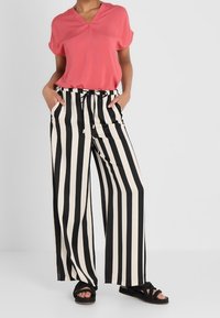 Top rosa de manga corta con escote en V, combinado con pantalones de pierna ancha a rayas blancas y negras de cintura alta. Sandalias negras completan el look.