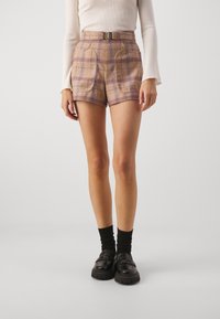 Shorts à carreaux marron avec des lignes violettes, dotés d'une taille haute et de plis. Associés à des chaussettes noires et des mocassins noirs épais.