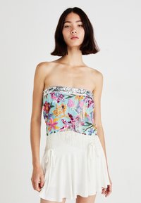 Kleurvolle geborduurde strapless top met bloemenpatronen, zilveren kraalaccenten en franjes aan de onderkant, gecombineerd met een witte luchtige rok.