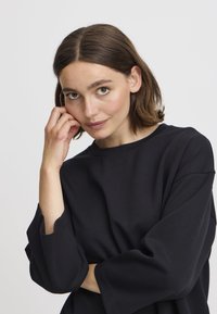 Felpa nera oversize con scollo a giro e maniche larghe. Texture morbida e design minimalista.