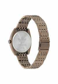 Pronksist roostevaba terasest kell geomeetrilise korpuse disaini, kudumisega rihma ja poleeritud korpuse tagaküljel graveeritud Adidas logo.