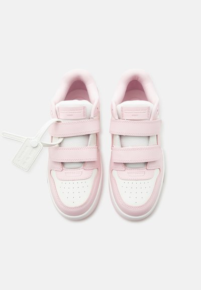 Paire de baskets roses et blanches avec double fermeture velcro, zone perforée au niveau des orteils, et une étiquette blanche attachée à la chaussure gauche.