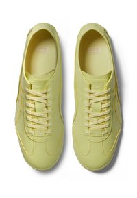 Vaaleankeltaiset tennarit, joissa on sileä pinta, erottuvat keltaiset tikkaukset, valkoiset nauhat ja pyöristetty kärki.