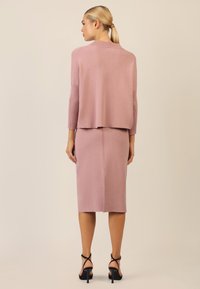 Rosa Strickpullover mit gerippten Akzenten und hohem Kragen, kombiniert mit einem passenden Bleistiftrock, der eine Rückennaht und einen geschlitzten Saum aufweist.