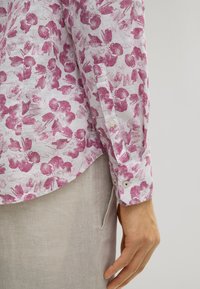 Langärmliges Hemd aus weißen Leinen mit einem rosa Blumenmuster, mit Knopfmanschetten und einem abgerundeten Saum.