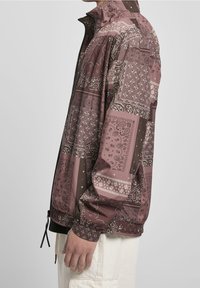 Leichte Zip-Jacke in Braun und Lila mit aufwendigen Bandana-Mustern. Verfügt über Bündchen und einen verstellbaren Saum für eine maßgeschneiderte Passform.