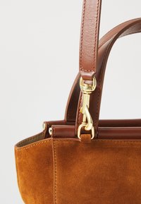 Hnedá semišová kabelka so štruktúrovaným tvarom, vybavená koženým popruhom, zlatými doplnkami a precízne prešitými okrajmi.