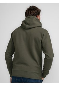 Bluza z kapturem w kolorze oliwkowej zieleni wykonana z miękkiego materiału. Posiada kieszeń kangurka, ściągacze na mankietach oraz luźny krój z widocznymi przeszyciami.