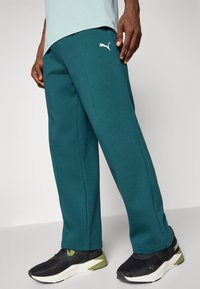 Søde, blandede bomulds sweatpants i en teal farve med en afslappet pasform, sidelommer og et hvidt Puma-logo på venstre lår. Sæt det sammen med sorte sneakers.