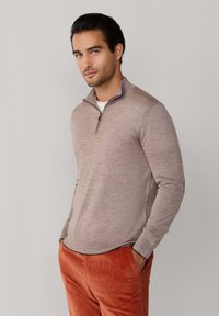 Lichtbruine ritstruien met een zachte brei textuur, voorzien van een staande kraag. Gecombineerd met roestkleurige corduroy broek.
