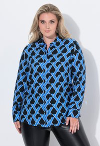 Sort bluse med blåt geometrisk mønster, lange ærmer, krave og knaplukning. Lidt løs pasform, båret med blanke sorte læderbukser.